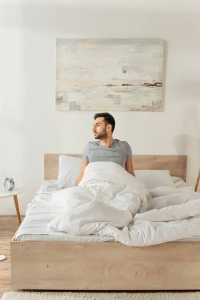 Seitenansicht eines bärtigen Mannes, der morgens zu Hause auf dem Bett sitzt — Stockfoto