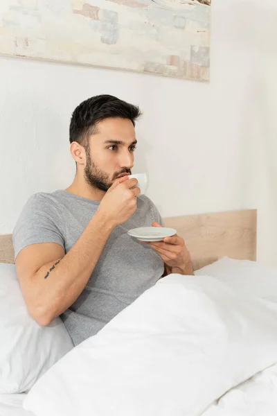 Татуированный мужчина пьет кофе в спальне дома — стоковое фото