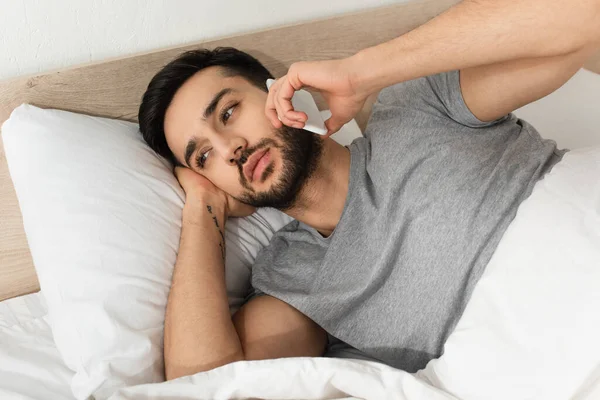 Бородатий чоловік розмовляє на мобільному телефоні, лежачи на ліжку — стокове фото