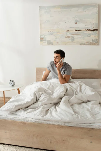 Amazed man talking on mobile phone in bedroom — Stock Photo