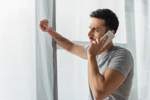 Vista laterale dell'uomo concentrato che parla sul telefono cellulare vicino alla finestra — Foto stock