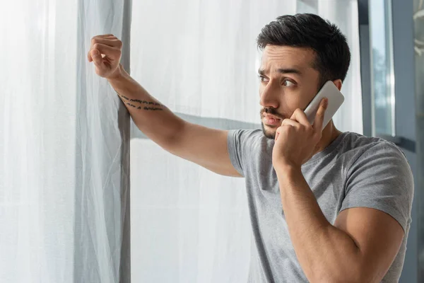 Hombre sorprendido hablando en el teléfono móvil y mirando a la ventana en casa - foto de stock
