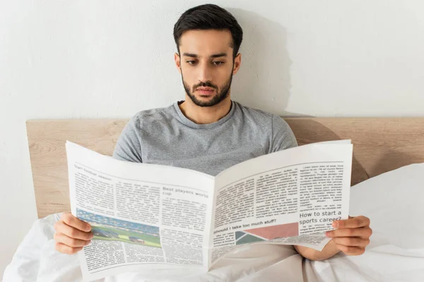 Uomo barbuto che legge giornale sul letto a casa — Foto stock