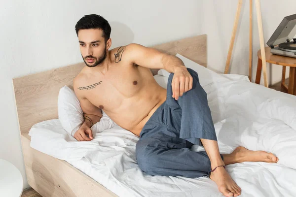 Hemdlos tätowierter Mann schaut morgens auf dem Bett weg — Stockfoto