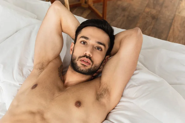 Vista dall'alto dell'uomo senza maglietta e barbuto che guarda la fotocamera sul letto — Foto stock