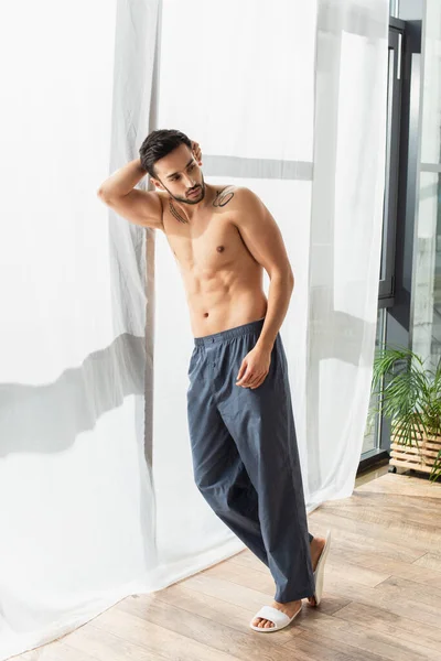 Shirtless man in slippers and pants standing near window — Stock Photo