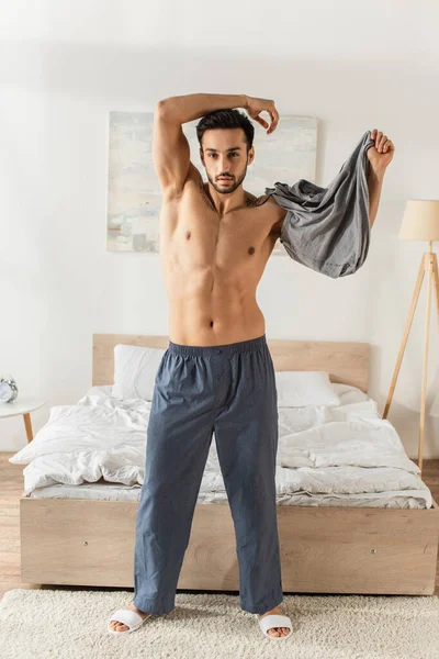 Hombre barbudo quitándose la camiseta en el dormitorio - foto de stock