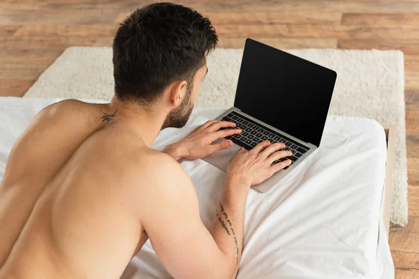 Overhead view of shirtless man using laptop with blank screen on bed — Stock Photo