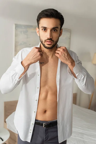 Tattooed man wearing white shirt and looking at camera at home — Stock Photo