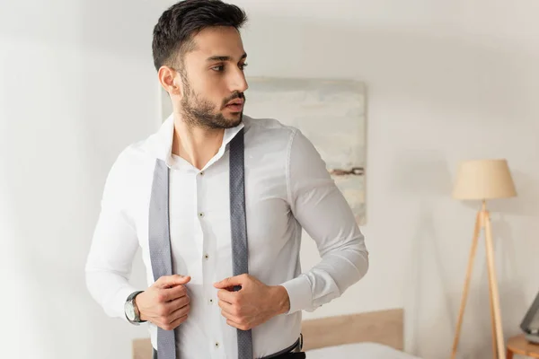 Bearded businessman in shirt holding tie at home — Stock Photo