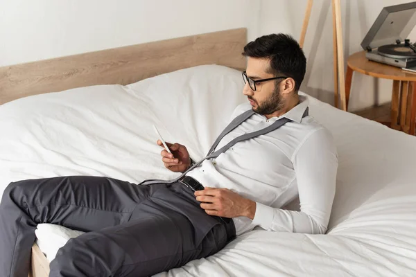 Seitenansicht eines bärtigen Geschäftsmannes mit Smartphone im Bett — Stockfoto