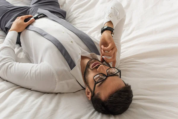 Високий кут зору бізнесмена в офіційному одязі, що говорить на мобільному телефоні на ліжку — стокове фото