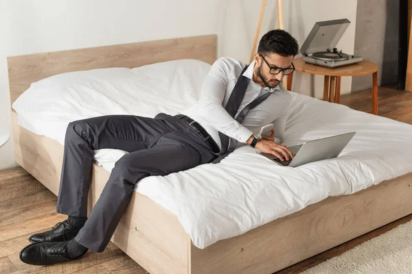 Homme d'affaires avec smartphone utilisant un ordinateur portable sur le lit à la maison — Photo de stock