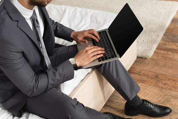 Vista recortada del hombre de negocios en traje usando el ordenador portátil con pantalla en blanco en la cama - foto de stock