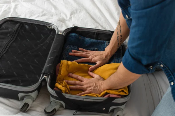 Vista cortada de homem pressionando roupas na mala na cama — Fotografia de Stock