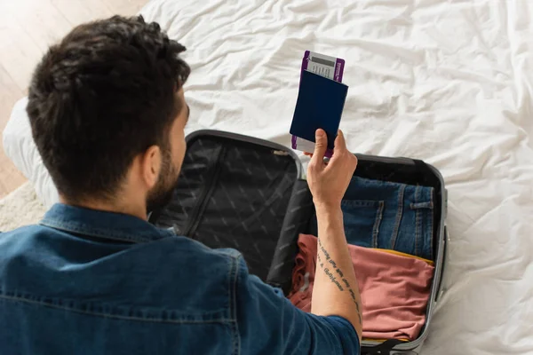 Overhead view of man holding passport with air tickets near suitcase at home — Stock Photo