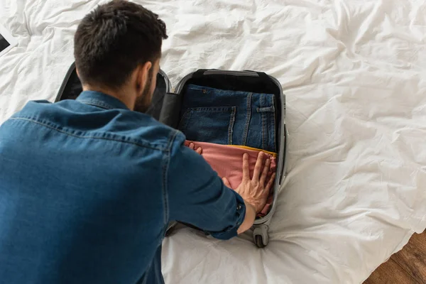 Visão aérea do homem colocando panos na bagagem na cama — Fotografia de Stock