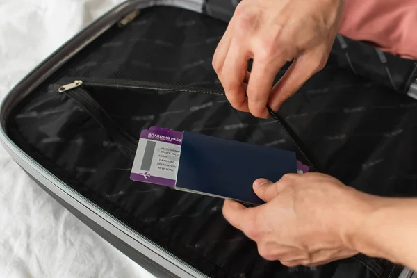 Cropped view of traveler putting boarding pass and passport in suitcase on bed — Stock Photo