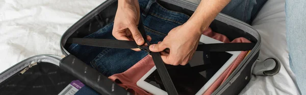 Cropped view of man locking belts of suitcase on bed, banner — Stock Photo