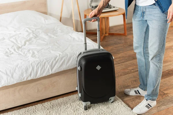 Cropped view of traveler holding suitcase in bedroom — Stock Photo