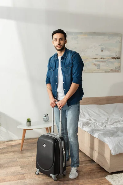 Jovem com mala olhando para a câmera no quarto — Fotografia de Stock