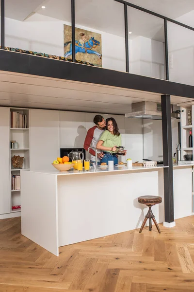 Smiling woman holding coffee pot near breakfast and boyfriend at home — Stock Photo