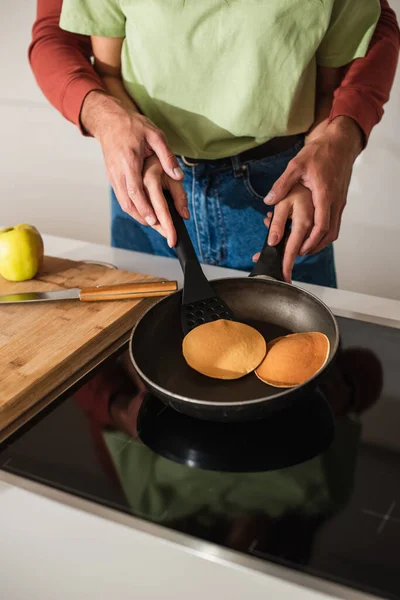 Cropped view of couple preparing pancakes near apple on cutting board in kitchen — Stock Photo