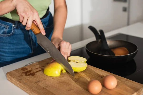 Cropped view of woman cutting apple near eggs on cutting board in kitchen — Stock Photo