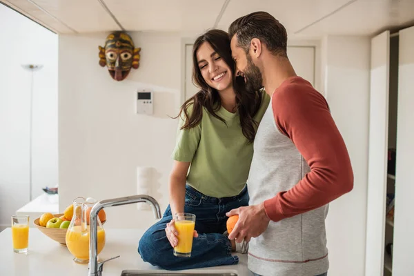 Couple souriant tenant jus et orange dans la cuisine — Photo de stock