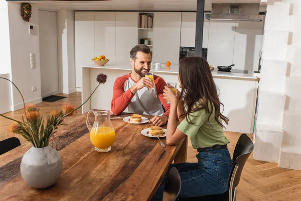 Homme souriant tenant un verre de jus d'orange près du petit déjeuner et de la petite amie — Photo de stock