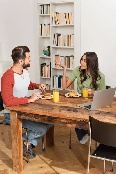 Mulher alegre conversando com namorado durante o café da manhã perto de laptop em casa — Fotografia de Stock