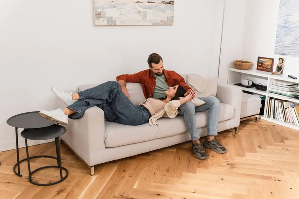 Femme souriante couchée près du petit ami sur le canapé à la maison — Photo de stock