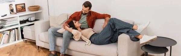 Mulher alegre segurando a mão do namorado enquanto deitado no sofá, banner — Fotografia de Stock