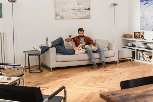 Lächelnde Frau mit Glas Wein auf Couch neben Freund liegend — Stockfoto