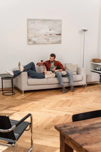 Smiling woman with glass of wine lying near boyfriend on couch at home — Stock Photo