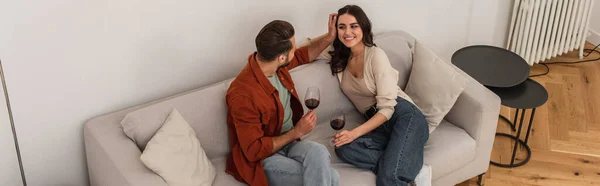 Vue aérienne de l'homme ajustant les cheveux de la petite amie souriante avec du vin à la maison, bannière — Photo de stock