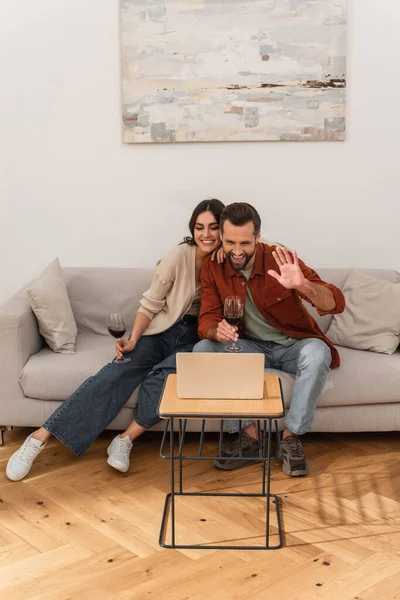 Casal sorridente com vinho tendo videochamada no laptop — Fotografia de Stock