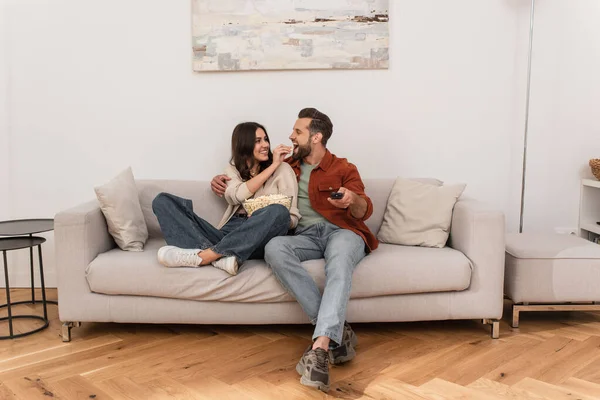 Smiling woman feeding boyfriend with popcorn at home — Stock Photo