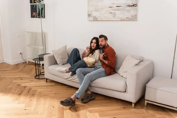 Scared coupe with remote controller and popcorn sitting on couch — Stock Photo