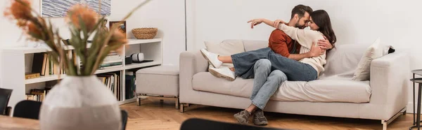 Вид сбоку молодой пары, обнимающейся на диване дома, баннер — стоковое фото