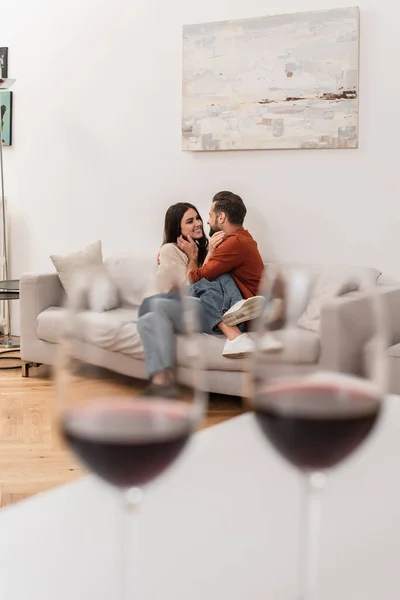 Mujer sonriente tocando novio cerca de copas de vino en primer plano borroso - foto de stock