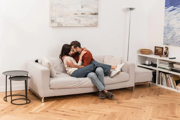 Seitenansicht eines lächelnden Paares, das sich zu Hause auf der Couch umarmt — Stockfoto