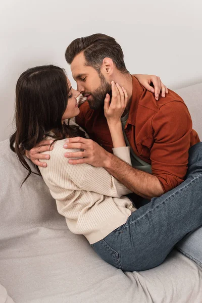 Vista lateral do jovem casal beijando e abraçando no sofá — Fotografia de Stock