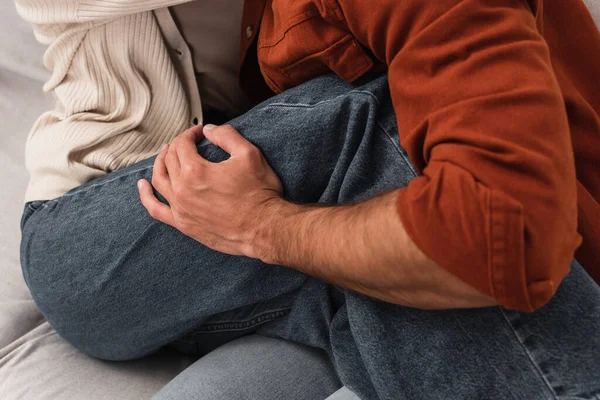 Vista cortada do homem tocando a perna da namorada no sofá — Fotografia de Stock