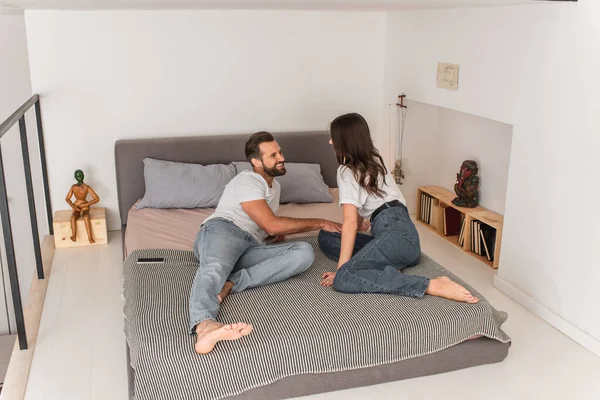 Homme souriant couché sur le lit près de petite amie et smartphone — Photo de stock