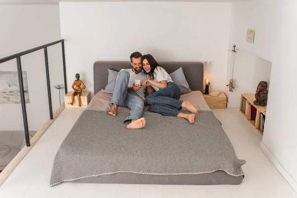 Улыбающаяся пара с помощью смартфона на кровати — стоковое фото