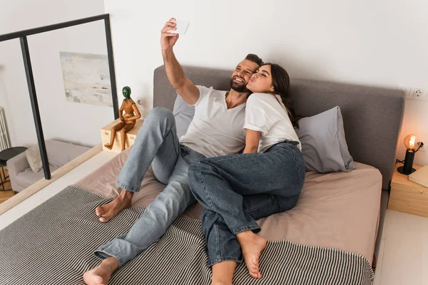 Couple joyeux prenant selfie sur téléphone mobile sur le lit — Photo de stock