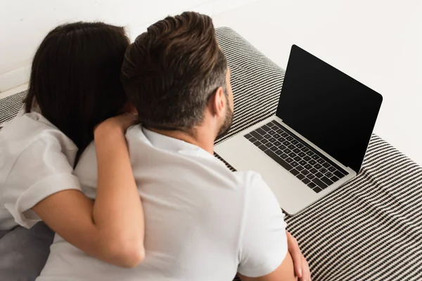 Вид ззаду молода пара лежить біля ноутбука з порожнім екраном на ліжку — стокове фото