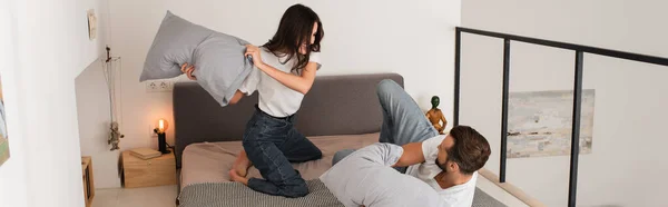 Young woman pillow fighting with boyfriend at home, banner — Stock Photo