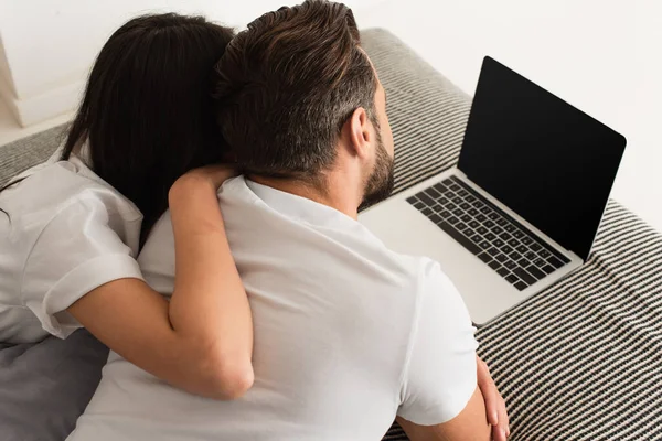 Вид женщины, обнимающей бойфренда рядом с ноутбуком с экраном на кровати — стоковое фото